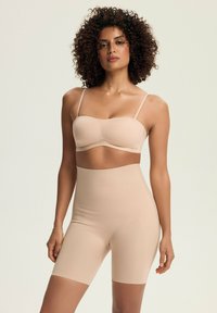 Nude seamless bralette with thin straps and matching high-waisted shorts, both made of soft, stretchy material, featuring a smooth texture.