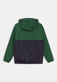 Grön och marinblå vindjacka med huva, elastiska muddar och åtsittande midja. Slätt, lätt material med färgblockdesign.