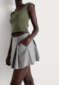 Olivově zelený, krátký rukávový crop top, který je kombinován se světlou šedou skort s plisováním a bočními kapsami, vyrobenou z hladkého materiálu.