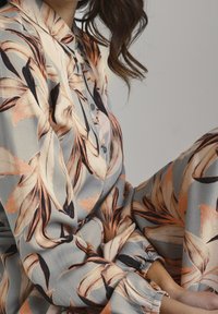 Blumenmuster auf seidig glänzendem Stoff in Grau-, Pfirsich- und Schwarztönen; besteht aus einem kragenlosen Hemd und elastischen Bündchen an der Hose.