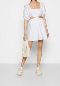 Vit miniklänning med puffärmar, skurna sidor och elastisk midja. Matchad med en beige handväska och sneakers med texturerade sulor.