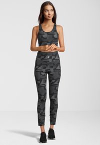 Completo sportivo nero composto da un top aderente e da leggings. Entrambi gli articoli presentano un motivo geometrico in diverse tonalità di grigio.
