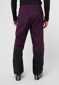 Pantaloni da sci in tessuto viola con una sezione inferiore nera, dotati di una tasca con zip e un design aerodinamico per mobilità e comfort.