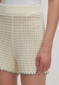 Gebreide crèmekleurige shorts met een open weefpatroon, voorzien van een geribbelde tailleband en een marineblauwe scalloped rand aan de onderzijde.