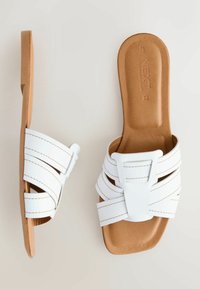 Sandales blanches à enfiler avec des brides croisées et des coutures blanches, présentant une forme d'orteil carrée et une semelle intérieure texturée de couleur beige.