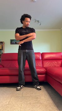 Raudonas odinis L formos sofa su lygiu paviršiumi. Šalia jos stovi žmogus juodu sportiniu marškinėliu ir tamsiomis džinsomis, pozavo.