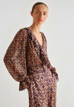 Blusa trasparente marrone con motivo astratto viola e oro, scollatura arricciata e maniche a sbuffo, abbinata a pantaloni con motivo coordinato.
