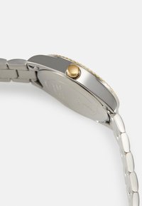 Silver metal watch showcasing a smooth case, a gold crown, and a polished bracelet with flat links. The design features a simple and modern aesthetic.