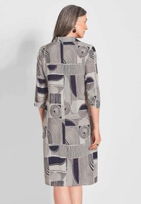 Druckkleid mit geometrischen Mustern in Marineblau und Beige. Es hat einen Kragen, drei Viertelärmel und endet in Oberschenkelhöhe.