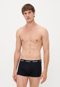 Calzoncillos bóxer negros de corte ajustado, con una suave cinturilla elástica marcada con 'HUGO' en texto blanco. Textura de tela de algodón suave.