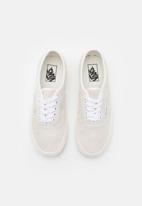 Baskets en daim gris clair avec lacets blancs, bout rond, semelle en caoutchouc blanc, et logo Vans noir sur la languette et le côté.