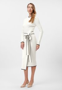 Knit midi dress in cream with contrasting black trim. Features a belted waist and long sleeves. Simple, sleek silhouette with a side slit.