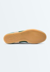 Semelle de chaussure plate avec une surface texturée de couleur marron clair et le nom de la marque "OYSHO" embossé près du talon, visible sur un fond blanc uni.