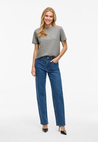 Grå t-shirt med korta ärmar kombinerad med höga raka jeans i blått. Märkbara spetsiga svarta högklackade skor kompletterar outfiten.