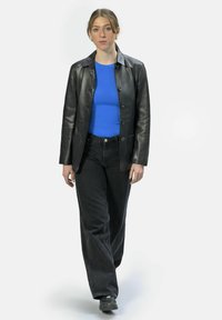 Zwarte leren jas over een blauw passend shirt, gecombineerd met zwarte wijde jeans en zwarte schoenen. Soepele textuur en op maat gemaakte ontwerp.