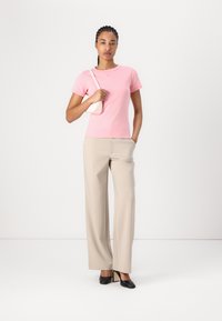 T-shirt en coton rose à manches courtes, associé à un pantalon large beige et des chaussures à talons noires. Design simple sans motifs visibles.