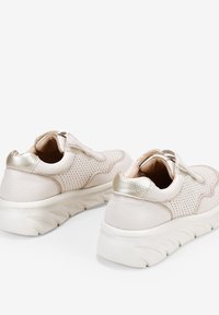 Zapatillas de deporte rosa claro con cuero perforado texturizado y acentos metálicos dorados. Suela blanca gruesa con patrón de olas y cuello acolchado.
