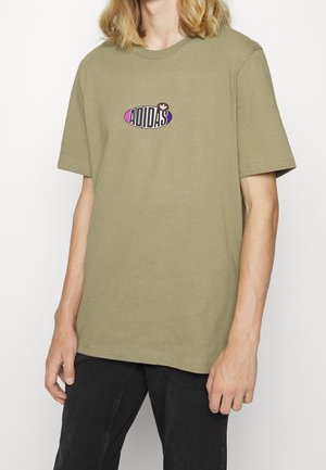 Olive green cotton t-shirt with short sleeves, featuring a black and purple oval logo that reads "ADIDAS" at the center.