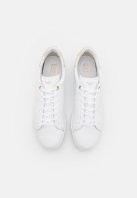 Para białych niskich sneakersów z złotymi oczkami i logo, starannie zawiązanych, wyeksponowana na jednolitym białym tle.