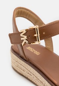 Sandale compensée en cuir marron avec semelle en jute tressée, boucle dorée avec logo MK et bride de cheville ajustable.