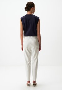 Navy cropped top met korte mouwen gecombineerd met witte gestreepte broeken. Model draagt witte hakken; achtergrond is neutraal en minimaal.