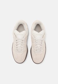 Beige suede sneakers with a textured upper, padded collar, and white laces. Rubber outsole features a brown tread pattern.