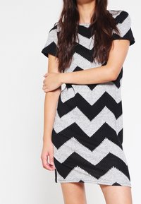Vestito a maniche corte con un motivo a zigzag grigio e nero, realizzato in tessuto morbido, con una vestibilità rilassata e scollatura rotonda.