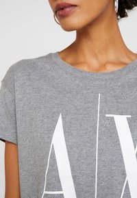 Šedé bavlněné tričko s kulatým výstřihem a krátkým rukávem; na přední straně se nachází velké bílé nápisy; hladká textura.