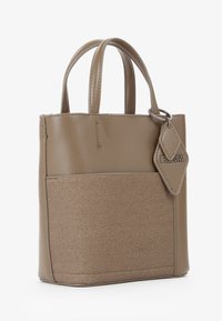 Piccola borsa taupe con doppi manici superiori, tasca frontale in tessuto e etichetta in pelle a forma di diamante attaccata da un anello metallico.