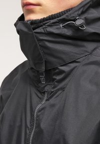 Czarna kurtka z wysokim kołnierzem, zamkiem z przodu i regulatorem na sznurku. Wykonana z gładkiej, lekkiej tkaniny o subtelnej fakturze.