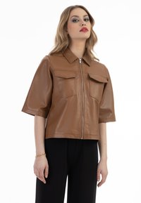Brun kunstlæder cropped jakke med korte ærmer, der har en lynlåslukning foran, to brystlommer og et klassisk kravedesign.