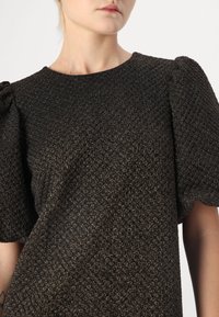 Top preto texturizado com mangas bufantes e decote redondo, apresentando um padrão sutil e brilhante por todo o tecido.