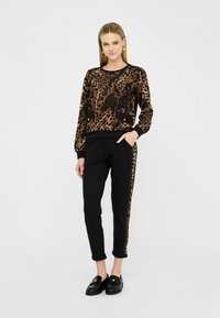 Felpa con stampa leopardata in tonalità marroni, abbinata a pantaloni neri a sigaretta con una riga leopardata laterale e scarpe slip-on nere.