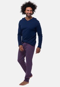 Granatowa koszulka z dekoltem w serek i długim rękawem zestawiona z piżamowymi spodniami w wielokolorowe paski, z pionowymi czerwonymi i niebieskimi paskami. Nosi się bez obuwia.