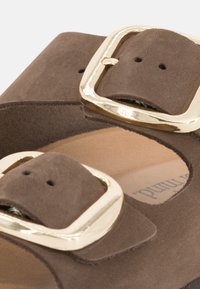Sandale en daim marron avec deux larges brides et de grandes boucles en or. Semelle intérieure en cuir naturel avec le nom de la marque imprimé. Forme ronde.