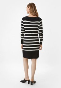 Schwarz-weiße gestreifte Kleid mit langen Ärmeln, rundem Halsausschnitt und unterem Abschnitt in einfarbigem Schwarz. Kombiniert mit schwarzen hohen Mules.