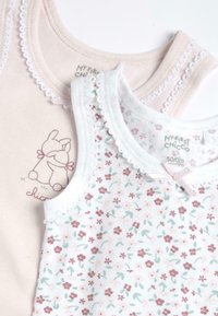 Deux débardeurs pour bébé empilés. L'un est rose clair avec un bord en dentelle et un motif de lapin. L'autre est blanc avec un motif floral et des accents de dentelle.