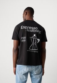 Black cotton t-shirt featuring white text reading "Espresso Awakening" and a graphic of a coffee maker on the back. Regular fit design.