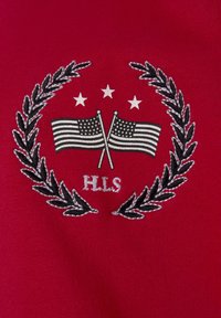 Red fabric featuring an embroidered emblem with two crossed American flags, a laurel wreath, three stars above, and the letters "H.L.S."