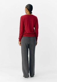 Pull rouge en maille avec des manches longues, associé à un pantalon large gris, mettant en avant une texture lisse et un design simple.