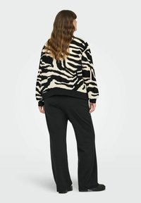 Zebra prugasta oversized jakna u crno-bijeloj boji s elastičnim manžetama, uparena s crnim širokim hlačama. Oba odjevna komada imaju opušteni kroj.