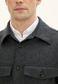 Grey wool button-up shirt jacket with a pointed collar, two chest pockets, and brown buttons. The fabric has a soft, textured finish.