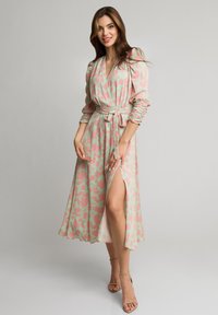 Kwiatowa sukienka w kolorze mięty z różowymi wzorami, z długimi bufiastymi rękawami, z paskiem w talii i szczeliną po boku. Gładki materiał z swobodnym krojem.