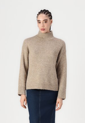 Pull à col roulé beige avec des poignets et un ourlet côtelés, fabriqué dans un tissu texturé doux. Associé à une jupe en denim bleu foncé.