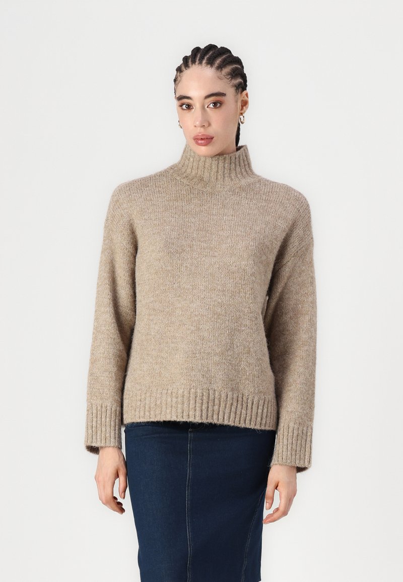 Beige polotröja med ribbad mudd och nederkant, tillverkad av ett mjukt texturerat tyg. Matchad med en mörkblå denimkjol.