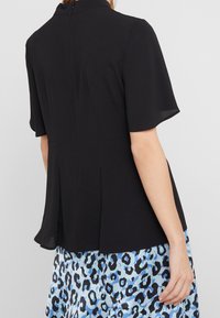 Czarna bluzka z krótkim rękawem i wysokim kołnierzem, ozdobiona zamkiem z tyłu oraz detalami w formie plis. Połączona z jasnoniebieską spódnicą w lamparcie cętki.