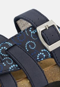 Marineblauwe sandalen met een patroonband met blauwe stippen, verstelbare metalen gesp en een kurken voetbed. Zachte suede-achtige afwerking.