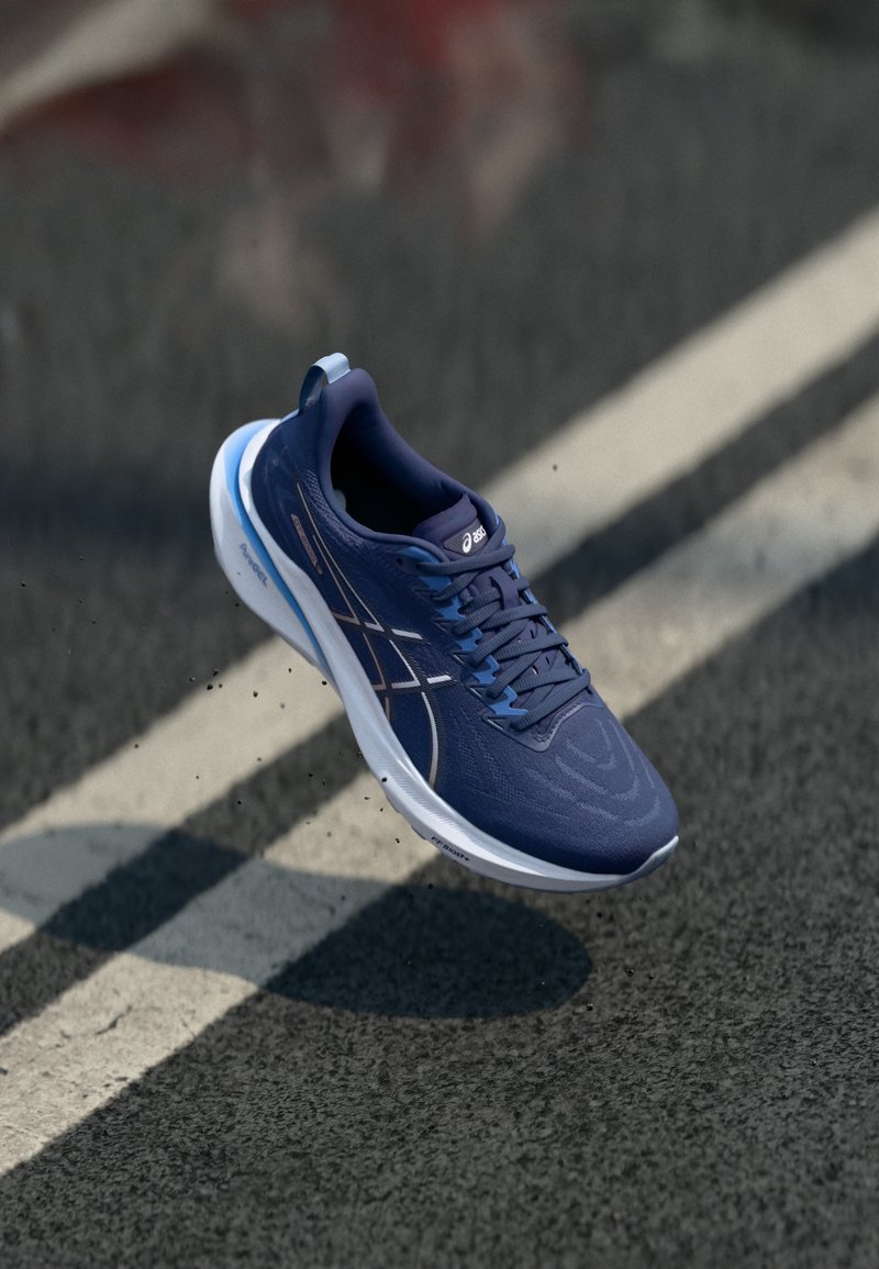 Chaussure de course avec une tige en maille bleu marine, au design épuré, semelle intermédiaire blanche et accents bleu clair. Présente une surface texturée et des lacets.
