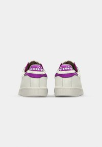 Un paio di sneaker in pelle bianca testurizzata con accenti viola e il logo "Diadora" visibile sulla linguetta del tallone, viste da dietro.