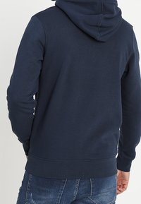 Sudadera azul marino hecha de una mezcla de algodón. Cuenta con un dobladillo y puños acanalados, con una gran capucha ajustable y una textura suave.